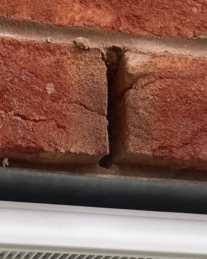 Red brickwork above a white window frame with a weep hole left open in the joint.