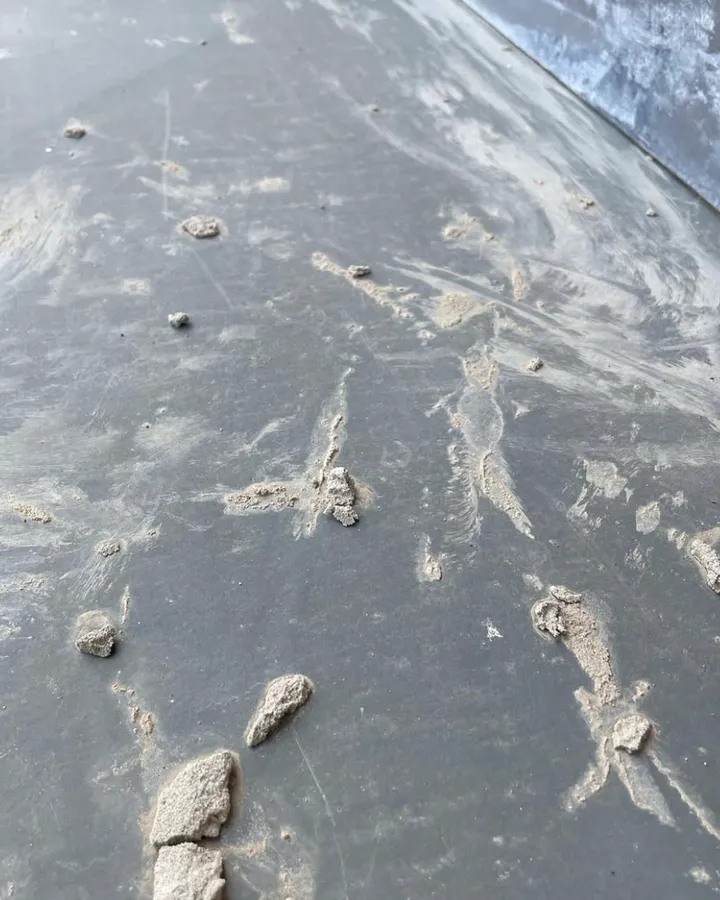 A dark grey lead surface marked with pale mortar splashes.