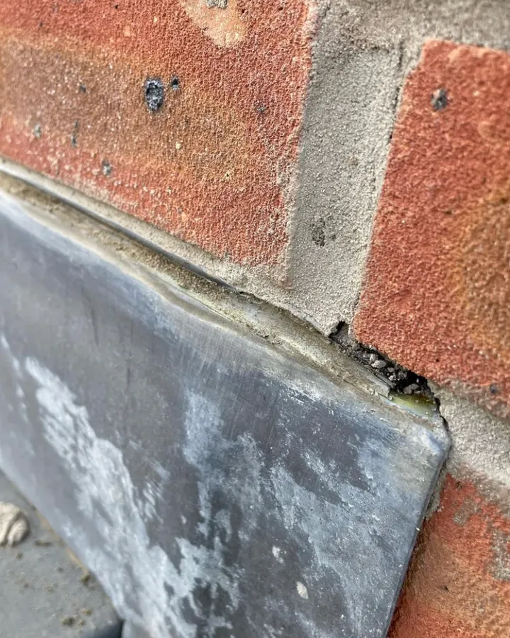 A lead flashing meeting red brickwork at a corner.