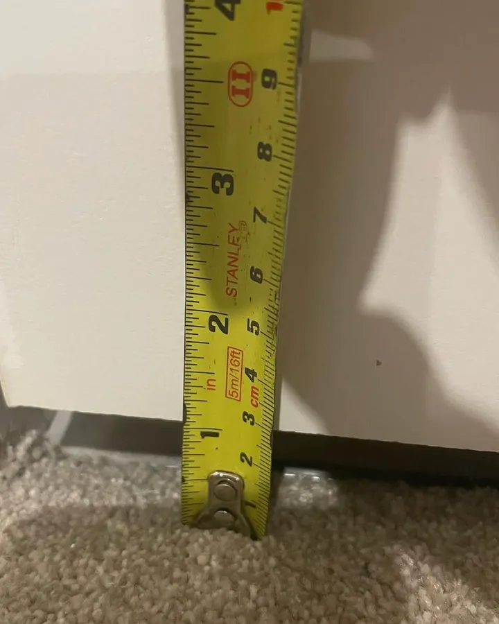 A tape measure standing on carpet against a white door frame showing a gap beneath the door.
