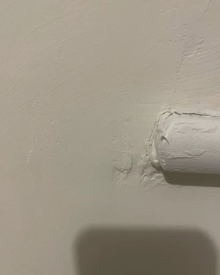 The rounded end of a painted window board against a plastered wall.