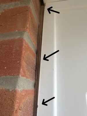 A white steel gallows bracket standing off a red brick wall, three arrows marking the gap.